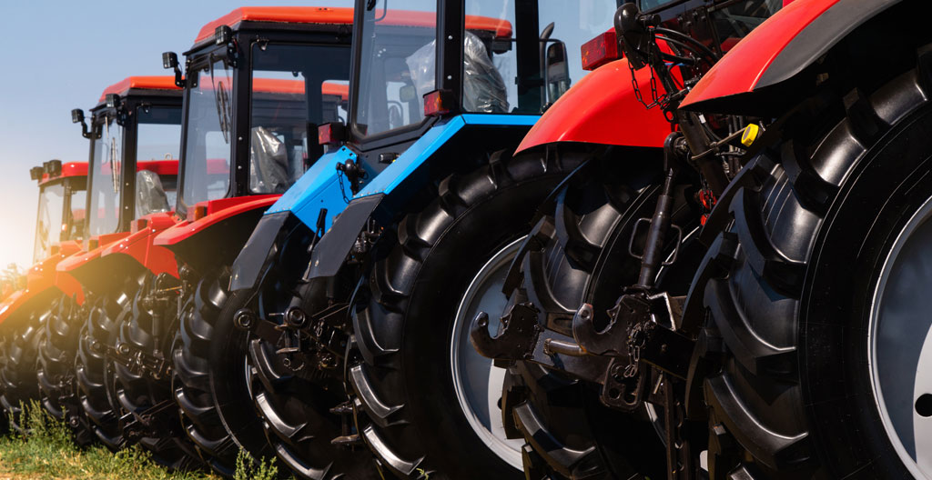Exploitant agricole et vendeur de concession en discussion devant une rangée de tracteurs d'occasion de différentes marques exposés sur le site d'une concession de matériel agricole