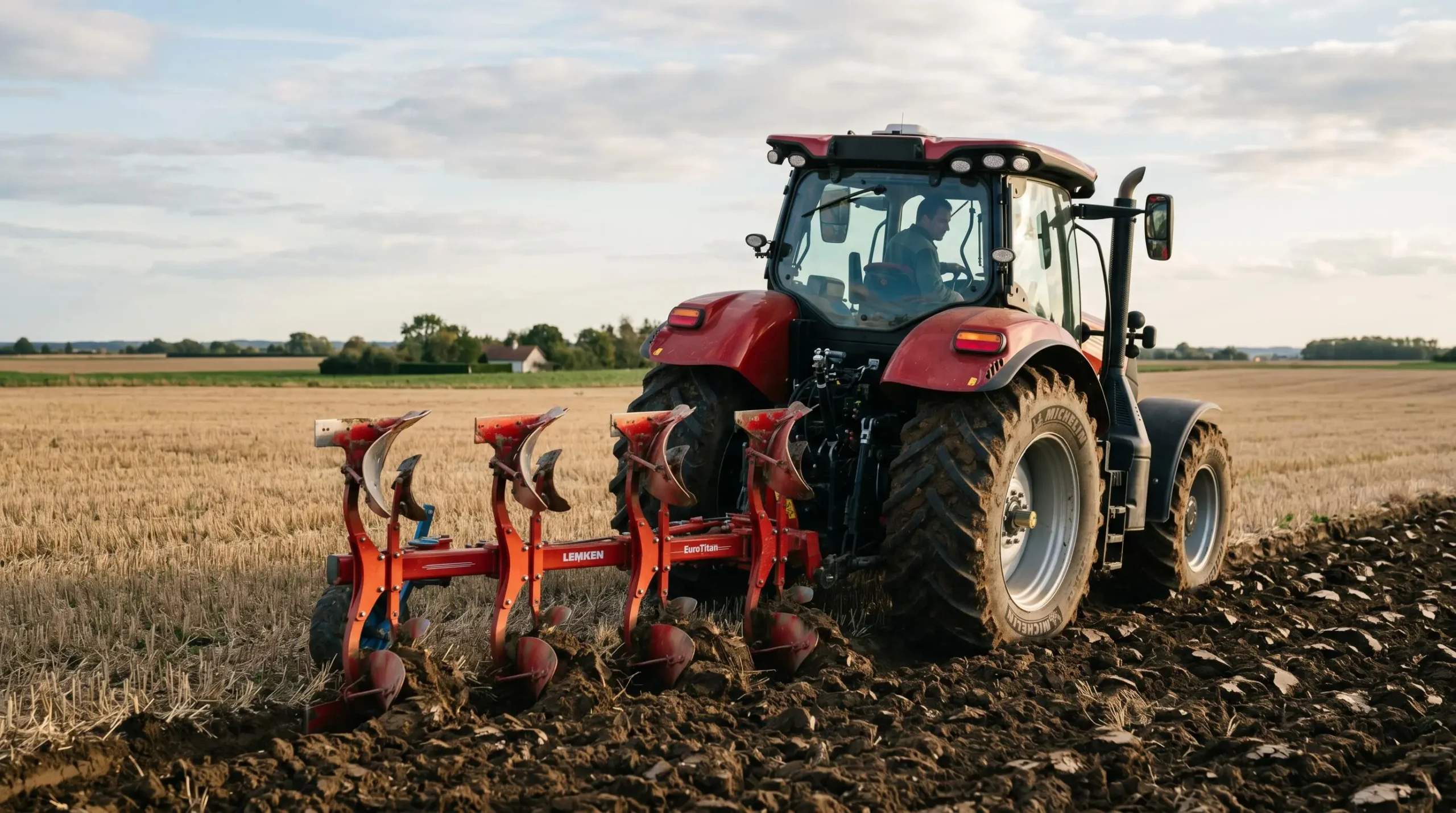 Tracteur agricole moderne avec cabine vitrée attelé à une charrue multi-socs labourant un vaste champ de céréales dans la plaine de Beauce, sous un ciel partiellement nuageux